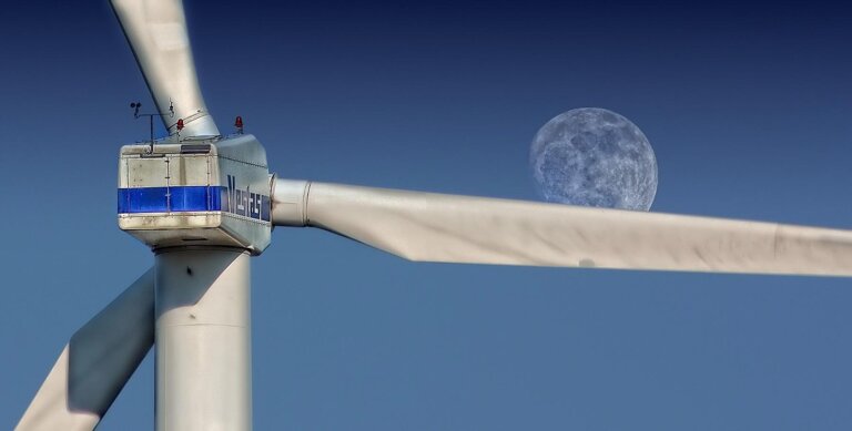 Nahaufnahme eines Windrads mit dem Mond im Hintergrund.